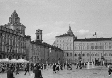 Vue monochrome de la Piazza Castello à Turin, en Italie, mettant en valeur l'architecture historique et la vie publique animée.
