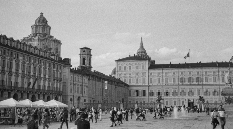 Vue monochrome de la Piazza Castello à Turin, en Italie, mettant en valeur l'architecture historique et la vie publique animée.