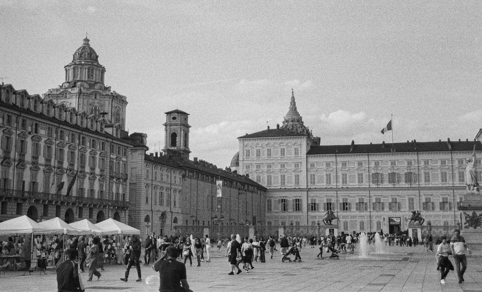 Vue monochrome de la Piazza Castello à Turin, en Italie, mettant en valeur l'architecture historique et la vie publique animée.