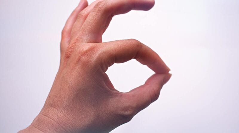 A close-up of a hand making an OK gesture, with a light background and soft lighting.